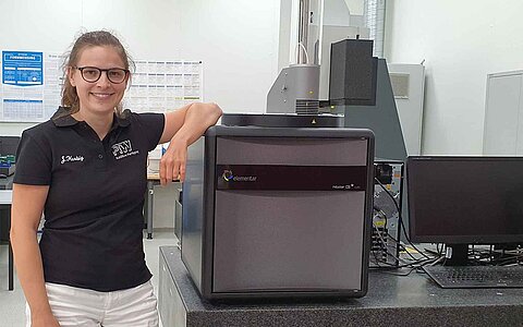 Woman beside an grey metal analyzer in the lab